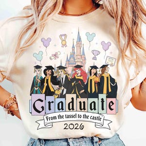 May include: Cream-colored t-shirt featuring a graduation design with Disney princess characters in graduation attire. The design includes a castle, balloons, and the text "Graduate From the tassel to the castle 2026".