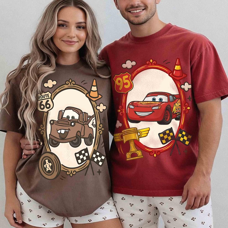 May include: Two people wearing matching t-shirts featuring cartoon car graphics. One shirt is brown with a tow truck, the other is red with a race car. Both shirts have a Route 66 and number 95 graphic.