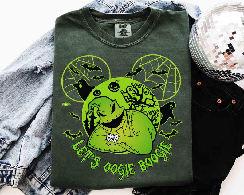 May include: Dark green t-shirt with a neon green graphic featuring a character from The Nightmare Before Christmas. The design includes bats, spiderwebs, and the text "Let's Oogie Boogie". The shirt is laid on a denim jacket and black pants.