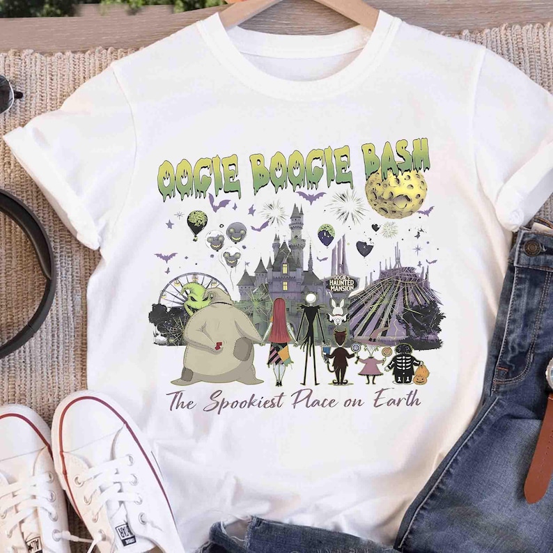 Puede incluir: Una camiseta blanca de manga corta con un estampado gr&aacute;fico que incluye el texto OOGIE BOOGIE BASH y The Spookiest Place on Earth. El dise&ntilde;o muestra un castillo, una luna, globos y varios personajes animados en un estilo oscuro.