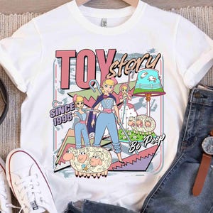 May include: White t-shirt with a colourful graphic of Bo Peep from Toy Story. The design includes the text "TOY story" and "SINCE 1995". The graphic has a cartoon style with Bo Peep and her sheep.