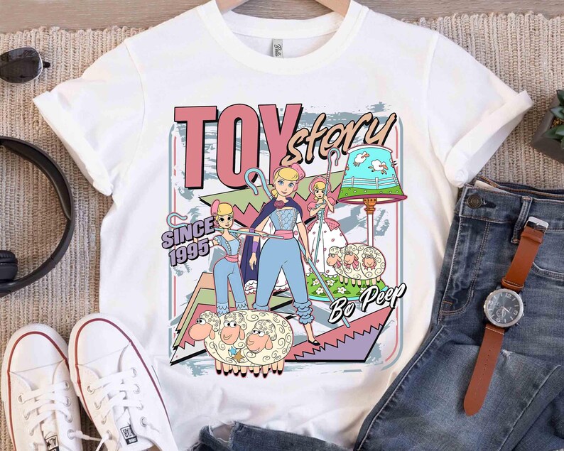 May include: White t-shirt with a colourful graphic of Bo Peep from Toy Story. The design includes the text "TOY story" and "SINCE 1995". The graphic has a cartoon style with Bo Peep and her sheep.