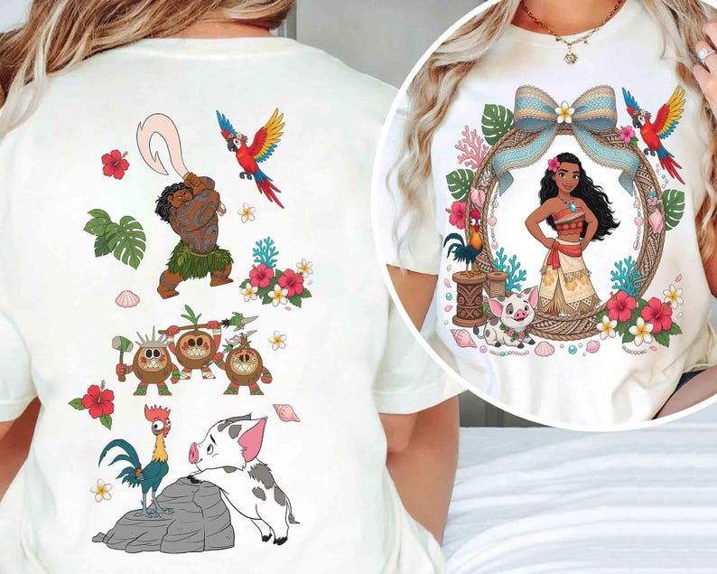 May include: A cream-colored t-shirt featuring a graphic print of Moana characters. The back displays Maui, Kakamora, a rooster, and a piglet with tropical flowers. The front circular design shows Moana framed by a bow, flowers, and a parrot.