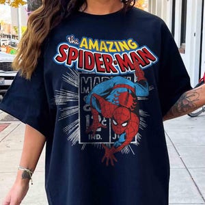 May include: Navy blue t-shirt with the words "The Amazing Spider-Man" in a comic book style. The graphic includes Spider-Man in his red and blue suit. The shirt has short sleeves.