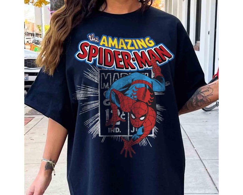 May include: Navy blue t-shirt with the words "The Amazing Spider-Man" in a comic book style. The graphic includes Spider-Man in his red and blue suit. The shirt has short sleeves.