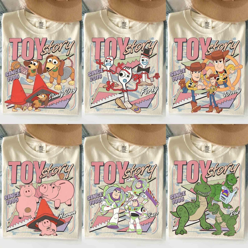 May include: Cream-coloured t-shirts featuring various Toy Story characters and the words "TOY STORY" in pink. Each shirt has a different character design, including Slinky Dog, Forky, Woody, Hamm, Buzz, and Rex. The shirts also have the text "SINCE 1995" or "SINCE 2019".