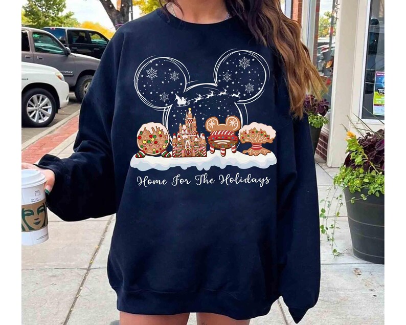 May include: Navy blue sweatshirt featuring a festive holiday design. The graphic includes a Mickey Mouse silhouette with snowflakes, a gingerbread castle, and the text "Home for the Holidays". The design incorporates gingerbread cookies and a sleigh.