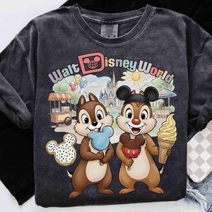May include: Dark gray t-shirt featuring Chip and Dale with ice cream cones and a Mickey Mouse cookie. The shirt has the words "Walt Disney World" in a colorful design, with a castle and other park elements.