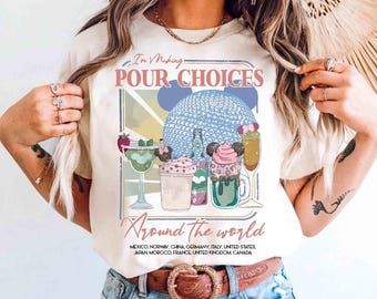 May include: Cream-colored t-shirt with the text "I'm Making POUR CHOICES Around the World." The graphic features a blue sphere, cocktails, and the names of several countries. The shirt has a crew neck and short sleeves.