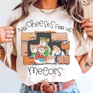 May include: Cream-coloured t-shirt with a cartoon illustration of mice inside a brick structure. The text "No Cheese For Us Meeees" is written above and below the illustration in a handwritten style. The mice are wearing various outfits.