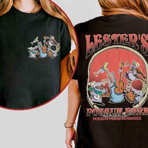 May include: Black t-shirt featuring a cartoon band of possums playing instruments. The front has a small graphic of the band, while the back displays a larger design with the text "Lester's Possum Park Possum Posse Jamboree."