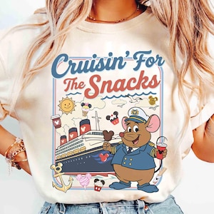 Pode incluir: Camiseta creme com um rato de desenho animado em uniforme de capit&atilde;o, segurando um picol&eacute; do Mickey Mouse e uma bebida. A camisa tem o texto "Cruisin' For The Snacks" com ilustra&ccedil;&otilde;es n&aacute;uticas e de comida, incluindo um navio de cruzeiro, sol e sorvete.