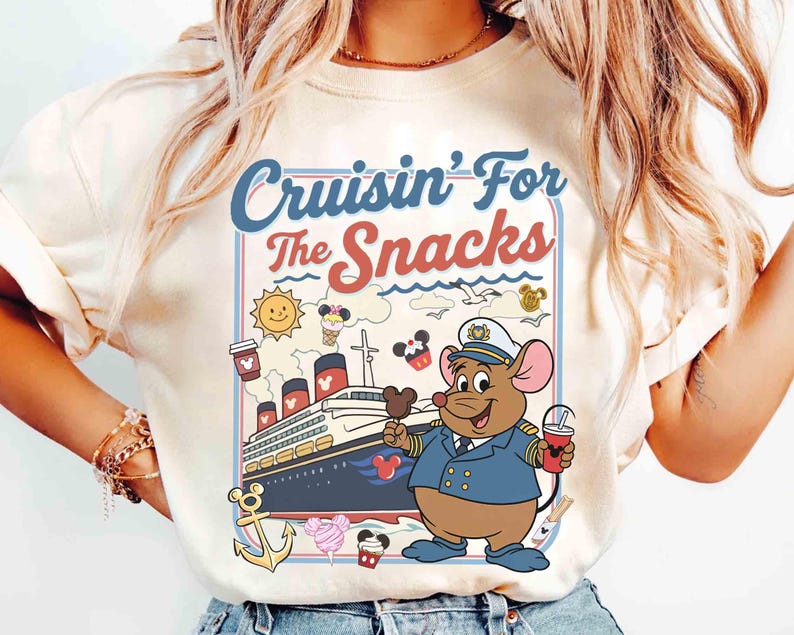 Pode incluir: Camiseta creme com um rato de desenho animado em uniforme de capit&atilde;o, segurando um picol&eacute; do Mickey Mouse e uma bebida. A camisa tem o texto "Cruisin' For The Snacks" com ilustra&ccedil;&otilde;es n&aacute;uticas e de comida, incluindo um navio de cruzeiro, sol e sorvete.