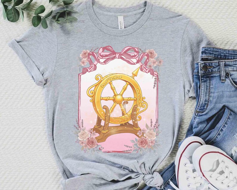 Puede incluir: Una camiseta gris con un dise&ntilde;o de tim&oacute;n dorado, detalles rosas y florales. El gr&aacute;fico est&aacute; enmarcado por una cinta rosa y flores. La camiseta se combina con vaqueros azules y zapatillas blancas.