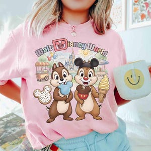 May include: Pink t-shirt with a colorful graphic featuring Chip and Dale holding ice cream treats in front of a Walt Disney World scene. The shirt also has the words "Walt Disney World" in pastel colors.