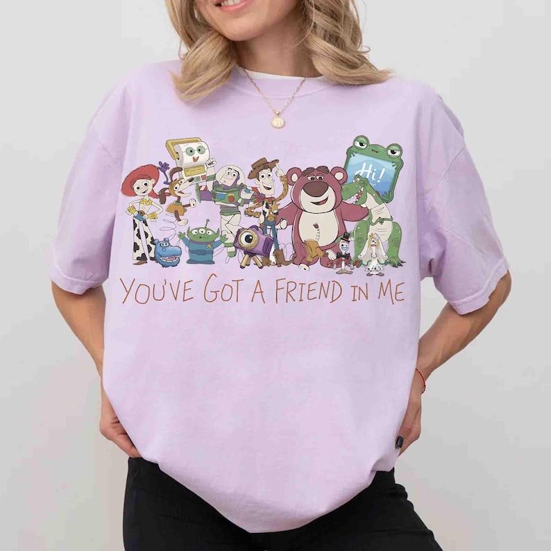 Op de afbeelding: Lichtpaars T-shirt met een kleurrijke afbeelding van Toy Story-personages. De tekst "You've Got a Friend in Me" staat in oranje letters onder de personages.