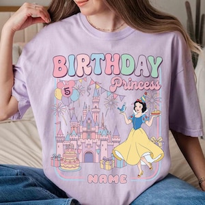 May include: Lilac t-shirt with a colourful graphic design. The design features the words "BIRTHDAY Princess" in bubble letters, a castle, and a cartoon of Snow White. The number 5 is displayed with balloons.