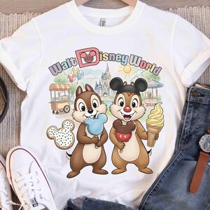 May include: White t-shirt featuring Chip and Dale holding treats in front of a Walt Disney World scene. The shirt includes the text "Walt Disney World" in a colorful design, along with a Mickey Mouse cookie.