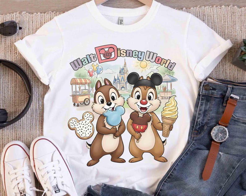 May include: White t-shirt featuring Chip and Dale holding treats in front of a Walt Disney World scene. The shirt includes the text "Walt Disney World" in a colorful design, along with a Mickey Mouse cookie.