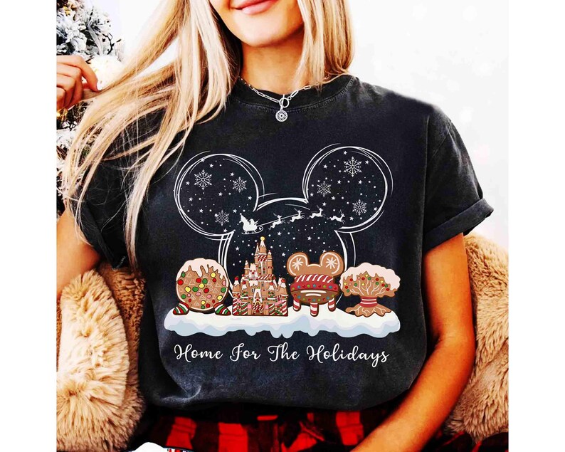 May include: Black t-shirt with a festive holiday design. The graphic features a Mickey Mouse head shape with snowflakes, a castle, and gingerbread characters. The text "Home For The Holidays" is printed below the design.