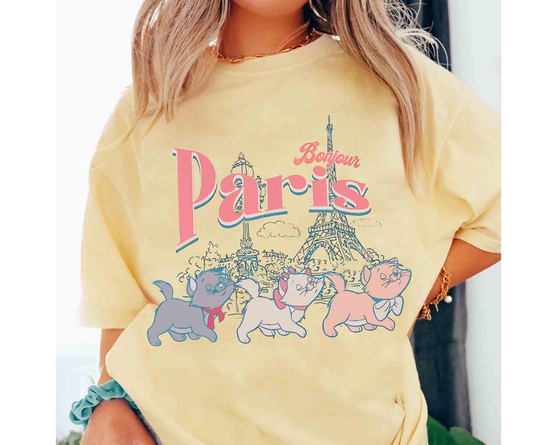 May include: Yellow t-shirt featuring the word "Paris" in pink and blue, with the Eiffel Tower and three cartoon kittens. The word "Bonjour" is above the word "Paris".