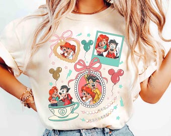 May include: Cream-colored t-shirt featuring cartoon characters in frames and a teacup. The design includes pink bows, Mickey Mouse balloons, and the word "ROXANNE" in a beaded chain. The characters are in a variety of poses.