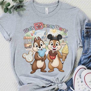 May include: A gray t-shirt featuring Chip and Dale with ice cream and a Mickey Mouse-shaped cookie, with the text "Walt Disney World" in a colorful font. The design includes a castle, sun, and food cart.