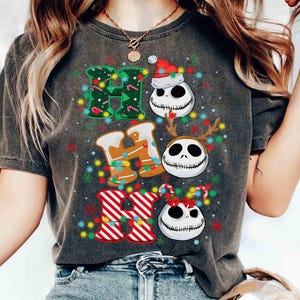 May include: Dark gray t-shirt featuring the words "HO HO HO" in a festive design. The letters are decorated with Christmas lights, candy canes, and Jack Skellington faces wearing a Santa hat, reindeer antlers, and a bow.