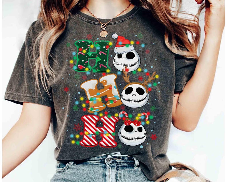 May include: Dark gray t-shirt featuring the words "HO HO HO" in a festive design. The letters are decorated with Christmas lights, candy canes, and Jack Skellington faces wearing a Santa hat, reindeer antlers, and a bow.