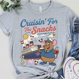 Pode incluir: Camiseta cinza com a frase "Cruisin' For The Snacks". O design apresenta um rato de desenho animado com uniforme de capit&atilde;o, segurando uma bebida e sorvete, com um navio de cruzeiro ao fundo.