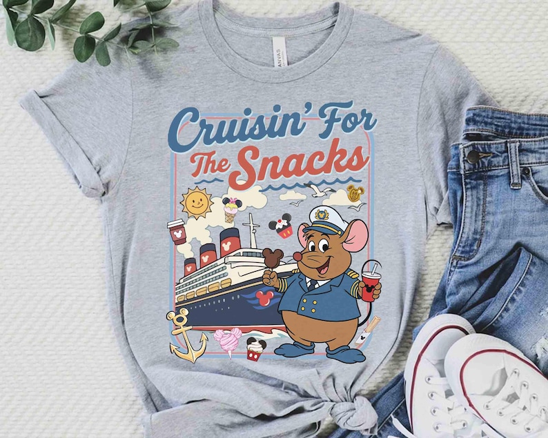 Pode incluir: Camiseta cinza com a frase "Cruisin' For The Snacks". O design apresenta um rato de desenho animado com uniforme de capit&atilde;o, segurando uma bebida e sorvete, com um navio de cruzeiro ao fundo.