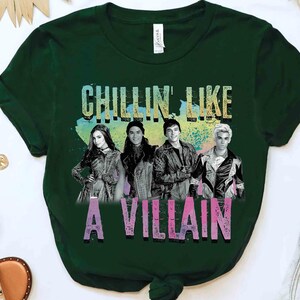 May include: Dark green t-shirt featuring a graphic of four people and the text "CHILLIN LIKE A VILLAIN" in colorful letters. The shirt is made of a soft material and has short sleeves.