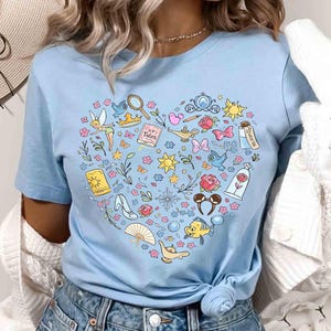 May include: Light blue t-shirt featuring a heart-shaped design filled with colorful illustrations of fairy tale elements. Includes a fairy, a magic lamp, a glass slipper, and the text "Fairy Tales".