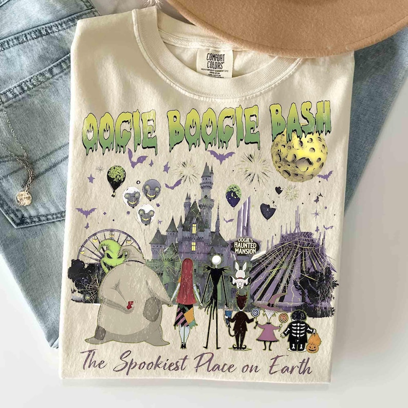 Puede incluir: Una camiseta de color crema con un estampado gr&aacute;fico que incluye el texto OOGIE BOOGIE BASH y The Spookiest Place on Earth. El dise&ntilde;o muestra un castillo, una luna, varios personajes de pel&iacute;cula, globos y fuegos artificiales.