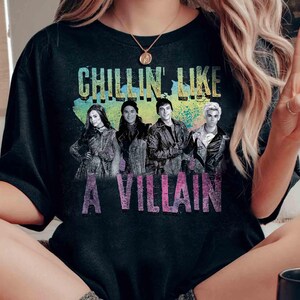May include: Black t-shirt with the text "CHILLIN' LIKE A VILLAIN" in a colorful design. The shirt features a graphic of four people. The shirt is made of a soft material.