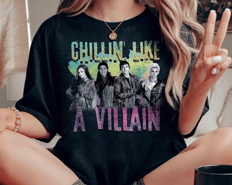 May include: Black t-shirt with the text "CHILLIN' LIKE A VILLAIN" in a colorful design. The shirt features a graphic of four people. The shirt is made of a soft material.