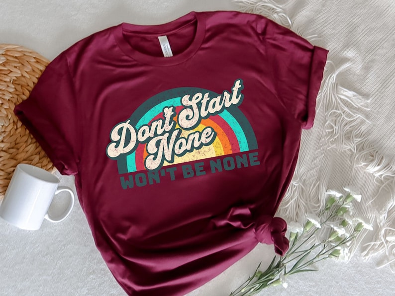 May include: A maroon t-shirt with a vintage rainbow graphic and the text "Don't Start None Won't Be None".