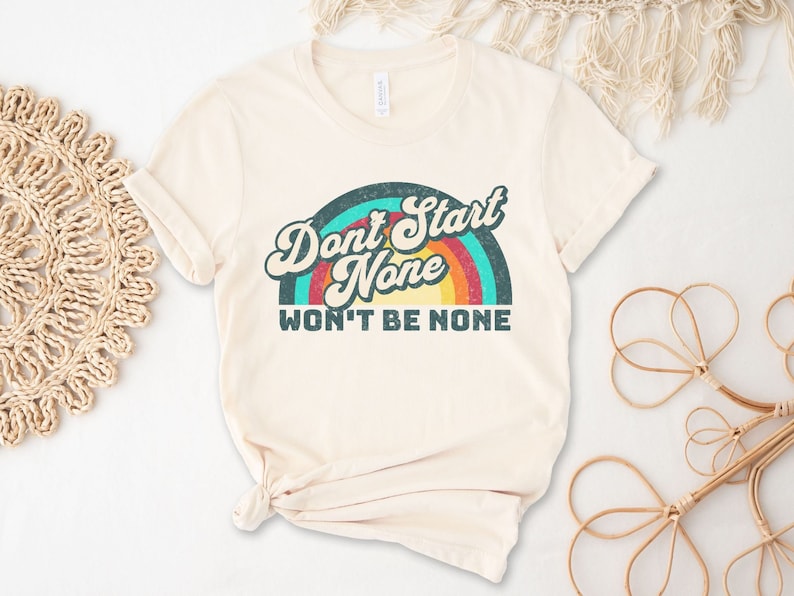 May include: A cream colored t-shirt with a retro rainbow graphic and the text "Don't Start None Won't Be None".
