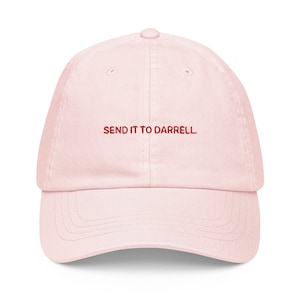May include: A pink baseball cap with the text "SEND IT TO DARRELL." embroidered in red on the front.