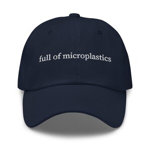 May include: A navy blue baseball cap with the embroidered text "full of microplastics" in white. The cap has a curved brim and a six-panel design, typical of a classic baseball hat.