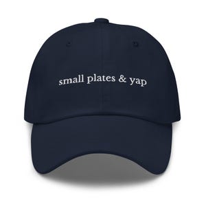 May include: A navy blue baseball cap with the text "small plates & yap" embroidered in white on the front.