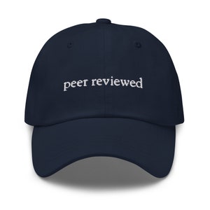 Può includere: Un cappello da baseball blu navy con il testo "peer reviewed" ricamato in bianco sul davanti.