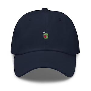 Puede incluir: Una gorra de béisbol azul marino con una imagen bordada de una caja de jugo verde con una pajita roja.