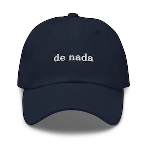 May include: A navy blue baseball cap with white embroidered text that reads "de nada".