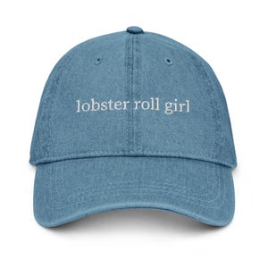 Peut inclure: Casquette de baseball en jean bleu clair avec le texte brodé "lobster roll girl" en blanc. La casquette a une visière incurvée et une sangle réglable à l'arrière. Un accessoire décontracté.