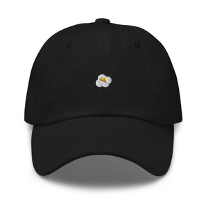 Puede incluir: Una gorra de béisbol negra con una palomita de maíz blanca y amarilla bordada en la parte delantera.