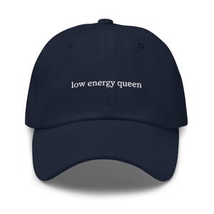 May include: A navy blue baseball cap with the text "low energy queen" embroidered in white on the front.