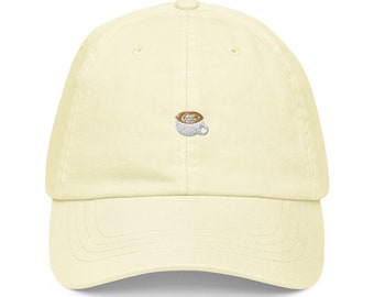 May include: A light yellow baseball cap with an embroidered image of a coffee cup with a brown liquid inside.