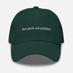 May include: A dark green baseball cap with the phrase "hot girls eat pickles" embroidered in white. The cap has a curved brim and an adjustable strap at the back. This hat is a fun accessory.