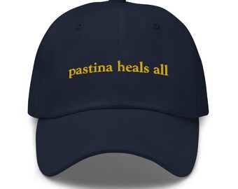 Puede incluir: Una gorra de béisbol azul marino con el texto "pastina heals all" bordado en amarillo.